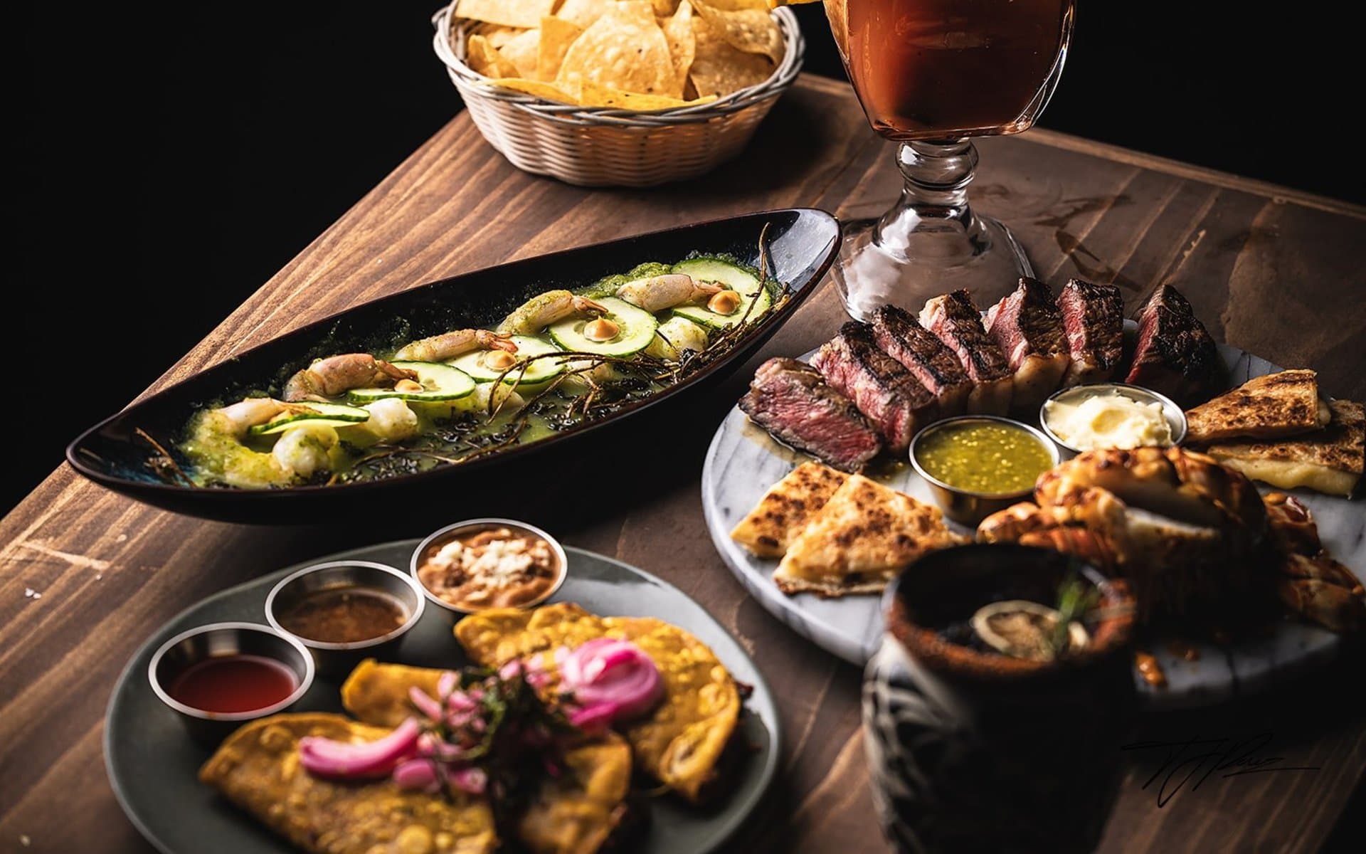 A table filled with Miel de Agave steaks, aguachile, tacos, and cocktails